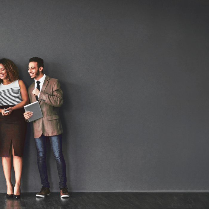 Four team members standing against a wall smiling and look at a screen together » admin by request